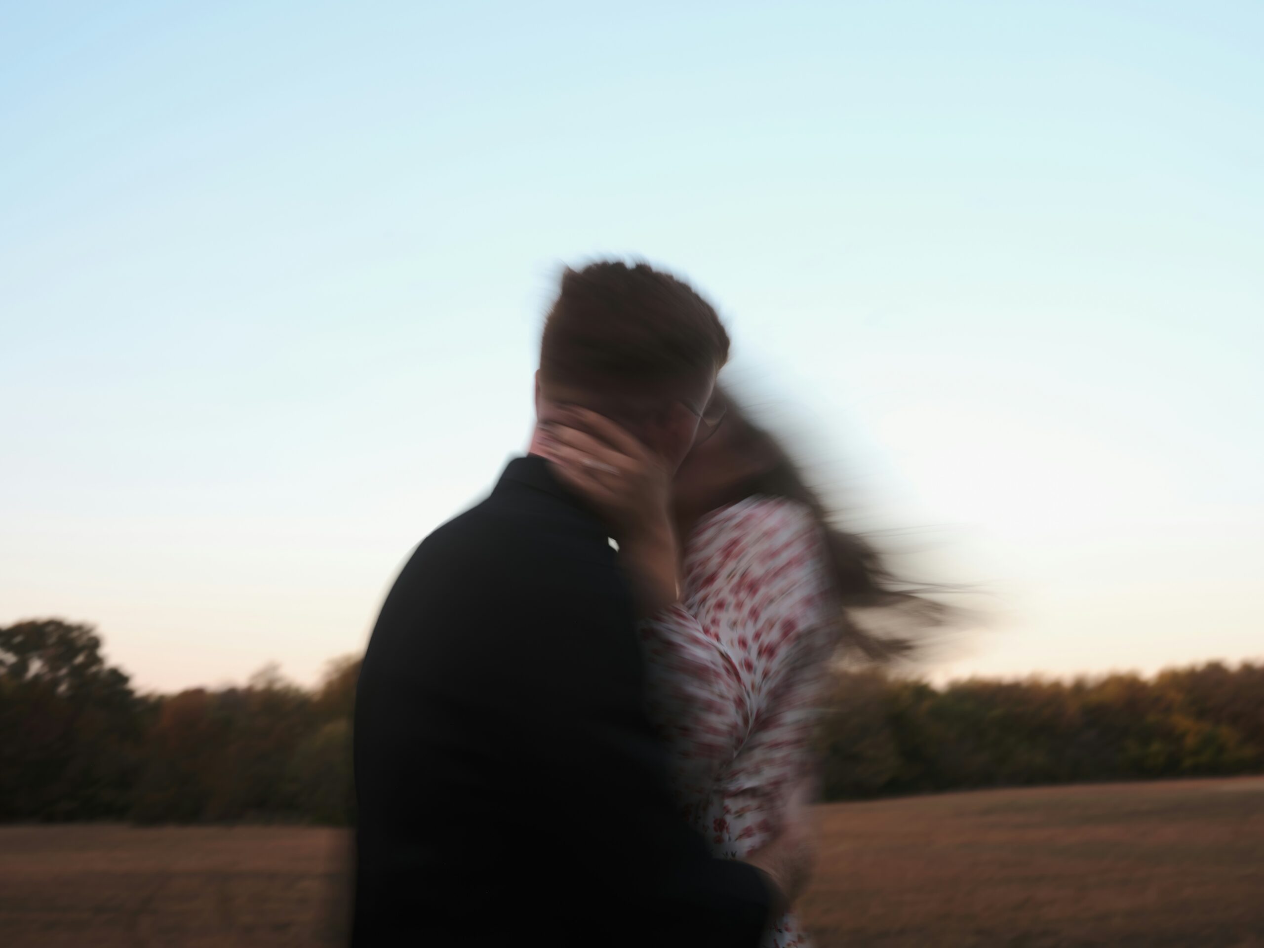 A blurry couple embraces and kisses outdoors.